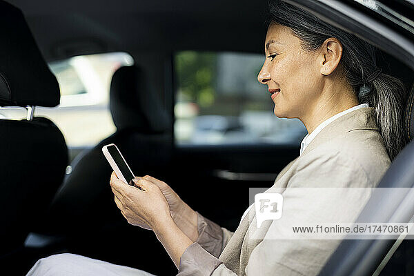 Mature woman using mobile phone while sitting in taxi
