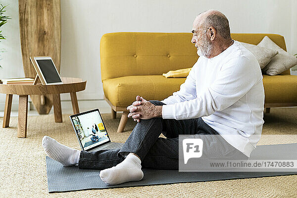 Älterer Mann schaut sich zu Hause Yoga-Tutorial über Laptop an