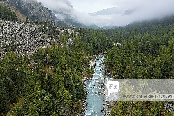 Drone view of Ova da Morteratsch river flowing through Val Morteratsch with thick fog in background