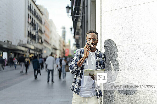 Smiling man with map talking on mobile phone at city street