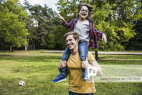 Happy man carrying playful boy on shoulders at park