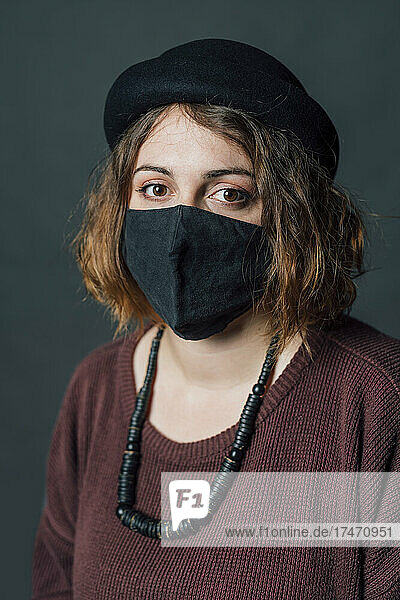 Woman with hat wearing protective face mask against gray background