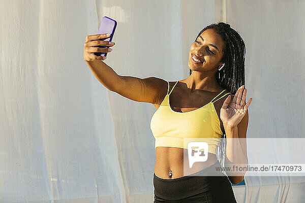 Happy sportswoman waving hand during video call through mobile phone