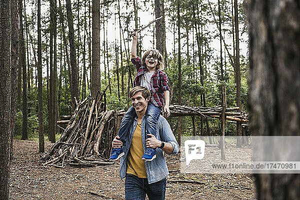 Happy father carrying son on shoulders in forest