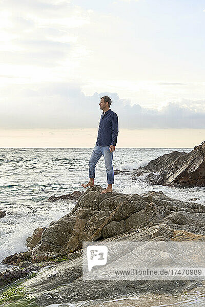 Man standing on rock by sea at sunset