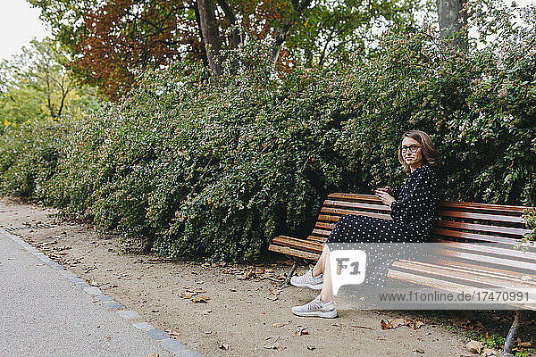 Smiling woman sitting on bench in public park