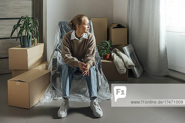 Young woman sitting on armchair wrapped in plastic at relocated home
