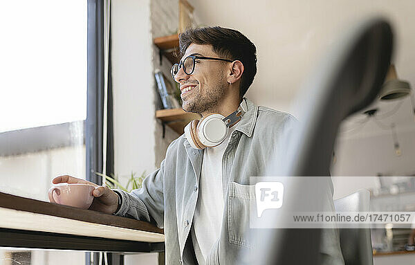 Lächelnder Geschäftsmann mit Kaffeetasse  der durch das Caféfenster schaut