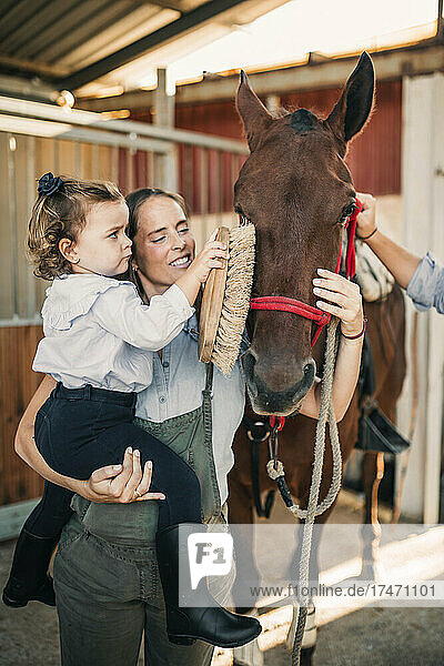 Mutter und Tochter putzen Pferd im Stall