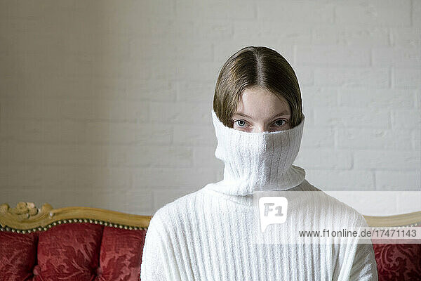 Teenagermädchen mit Gesicht  das von einem weißen Rollkragenpullover bedeckt ist