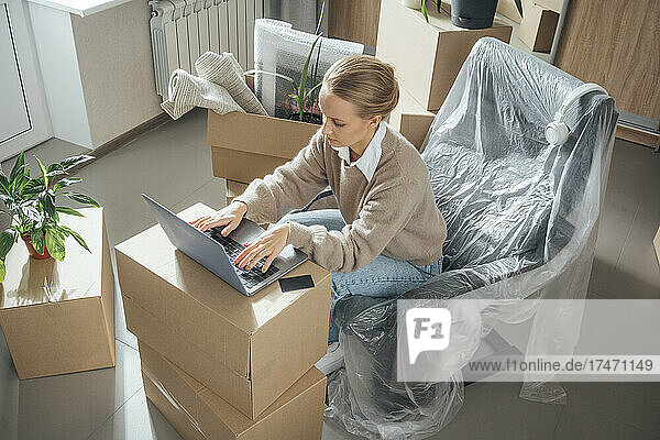 Young woman with laptop working at new home