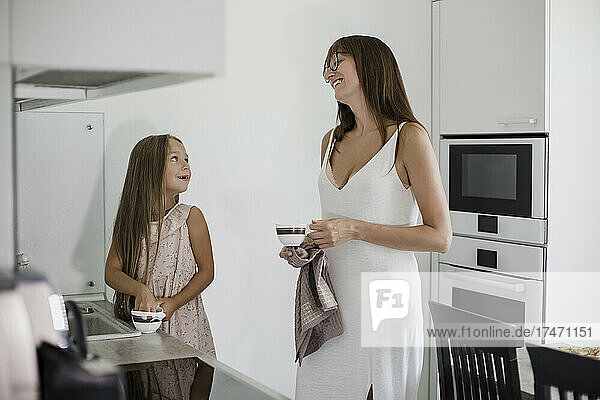 Smiling daughter helping mother cleaning cups in kitchen