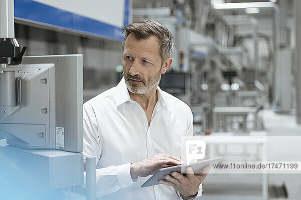 Geschäftsmann hält digitales Tablet in der Hand  während er Maschinen in der Fabrik betrachtet