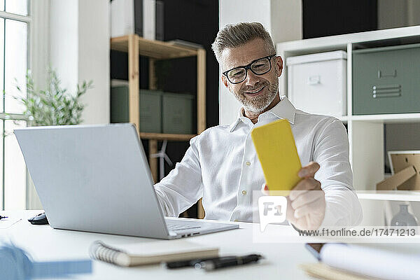 Lächelnder Geschäftsmann  der sein Mobiltelefon am Schreibtisch benutzt