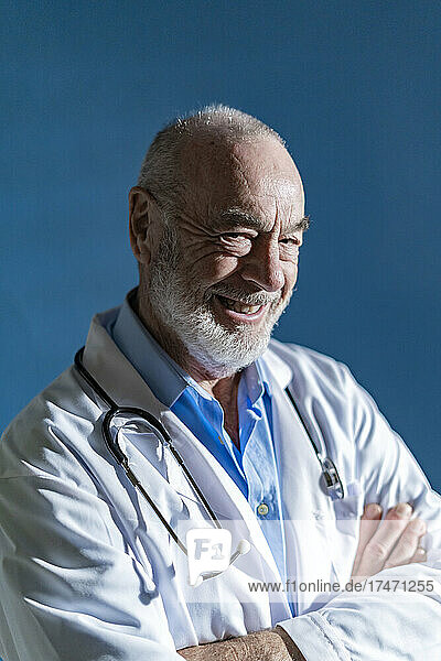 Happy doctor with arms crossed against blue background