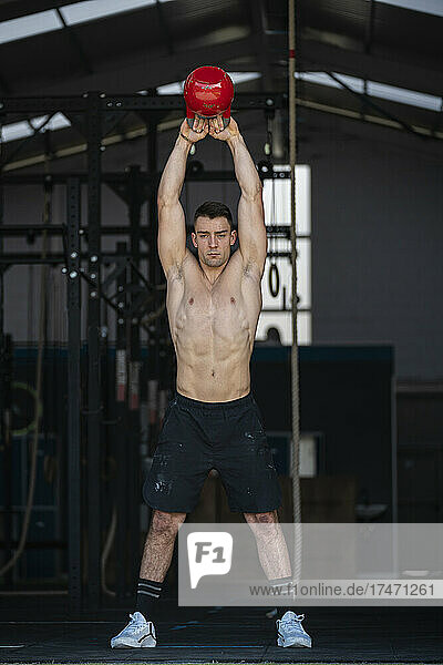 Confident male athlete exercising with kettlebell in gym