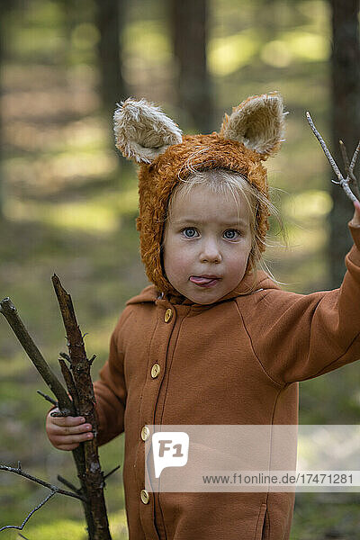 Nettes Mädchen mit Holzstöcken  die im Wald die Zunge herausstrecken