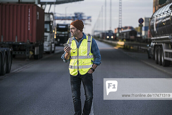 Male truck driver with smart phone walking on street at industry