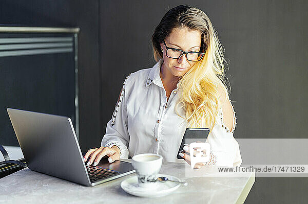 Blond businesswoman using mobile phone while working in cafe