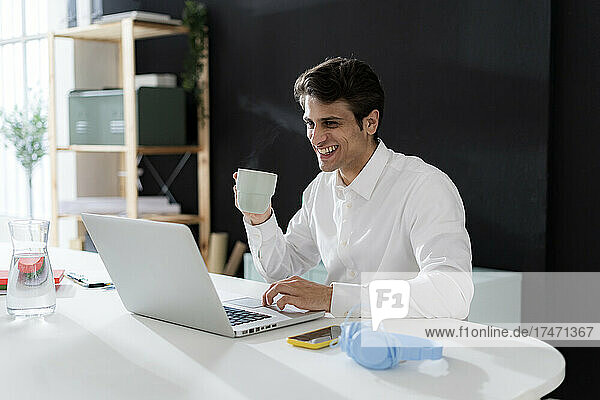 Smiling businessman having and using laptop at desk in office