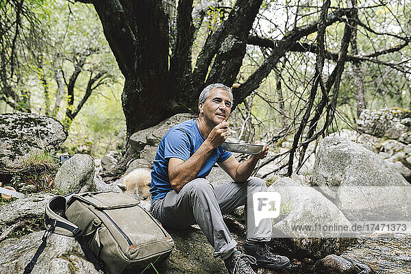 Mature male tourist eating food while sitting on rock