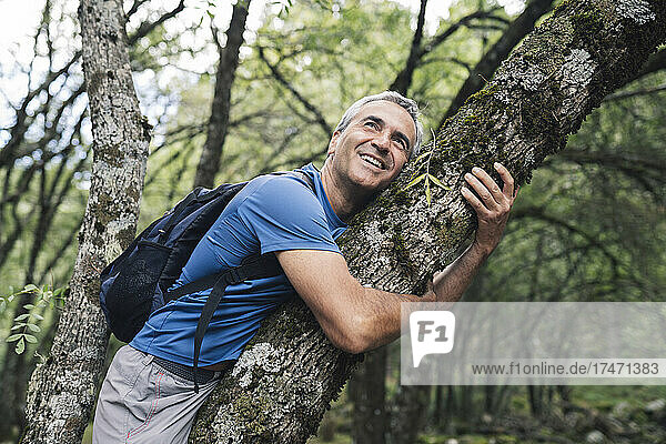 Mature man smiling while embracing tree trunk in forest