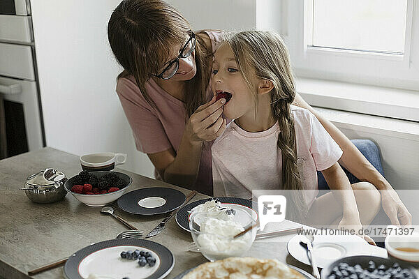 Mother feeding berry to daughter at table