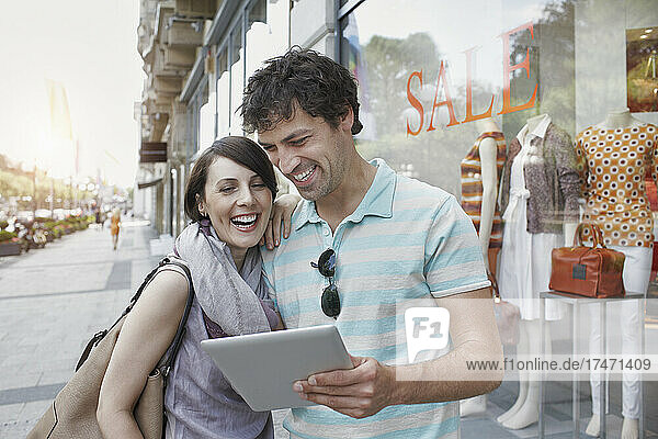 Cheerful couple using digital tablet while standing by clothing store