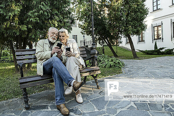Couple using sharing smart phone while sitting on bench