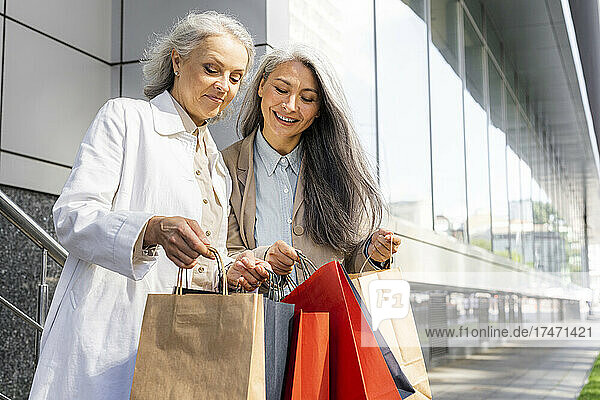 Mature women searching in shopping bags outside mall