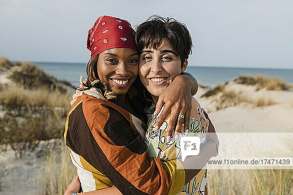 Happy young woman embracing girlfriend with bandana at beach