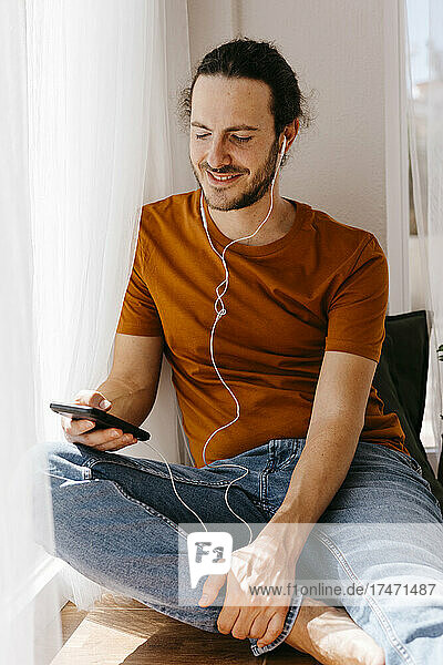 Man with mobile phone listening music through in-ear headphones at home