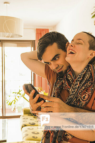Man using mobile phone while embracing woman at home