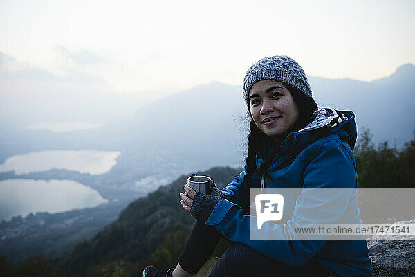 Smiling hiker with coffee mug sitting on mountain