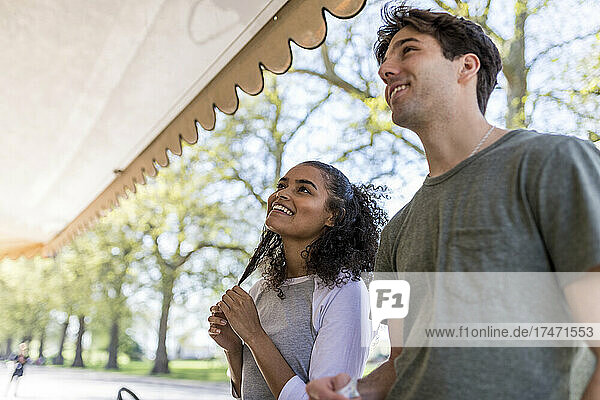 Young woman with hand in hair standing by man near ice cream stand