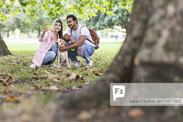Smiling woman taking selfie with dog and boyfriend in park