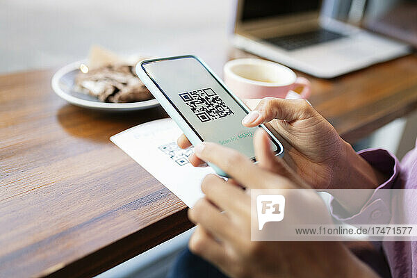 Woman scanning QR code through mobile phone at cafe table