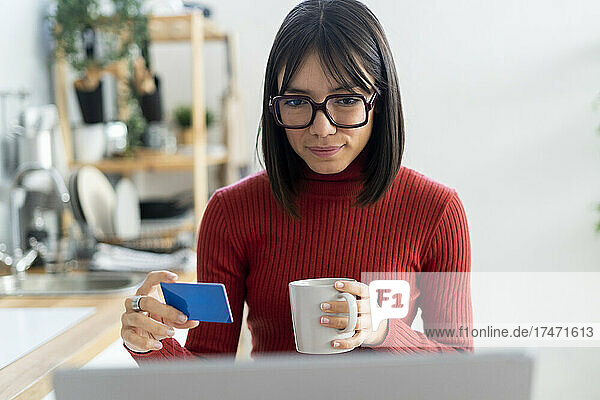Freelancer with credit card holding coffee mug looking at laptop