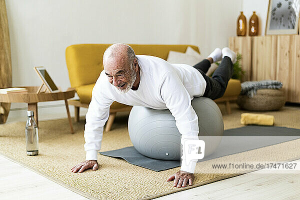Active senior man exercising on fitness ball at home