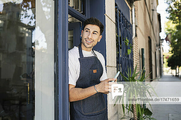 Owner with smart phone leaning on cafe door