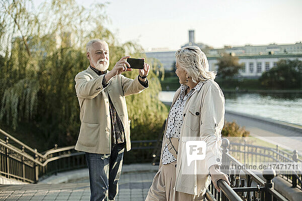 Mann fotografiert Frau per Smartphone  während er auf einer Brücke steht