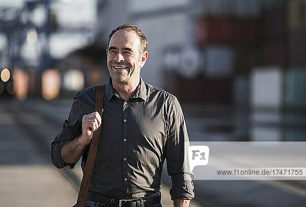Smiling businessman with shoulder bag walking on street