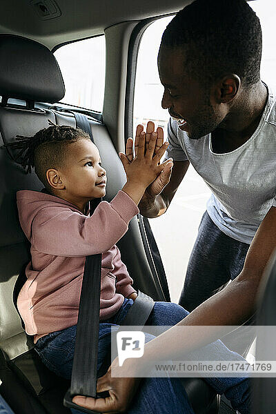 Father giving high-five to son while fastening seat belt in car