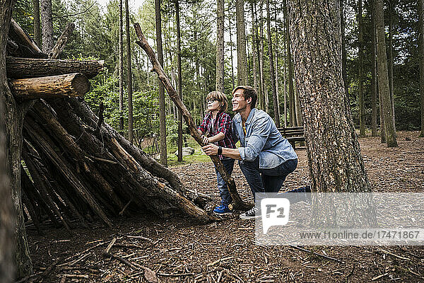 Boy helping father making log tent in forest