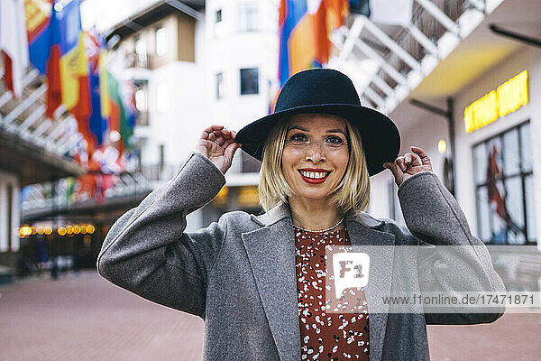 Lächelnde schöne blonde Frau mit Hut in der Stadt