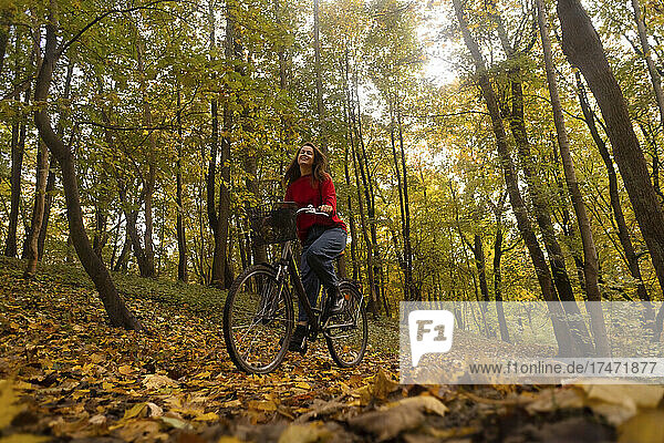 Woman cycling in front of trees at autumn park