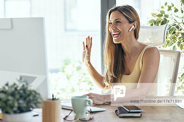 Happy businesswoman waving during video conference at home office