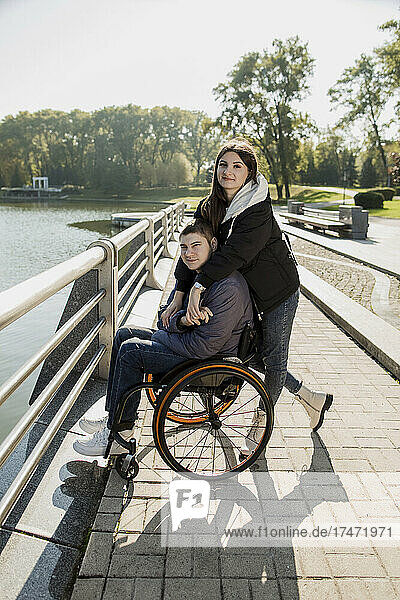 Woman embracing man sitting in wheelchair at embankment