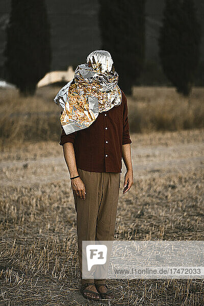 Man standing on grass with head wrapped in metallic foil