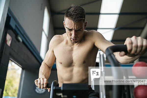Young shirtless male athlete on cross trainer in gym